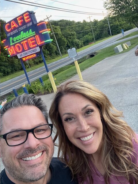 selfie of man and woman in front of neon sign showing importance of romantic getaways