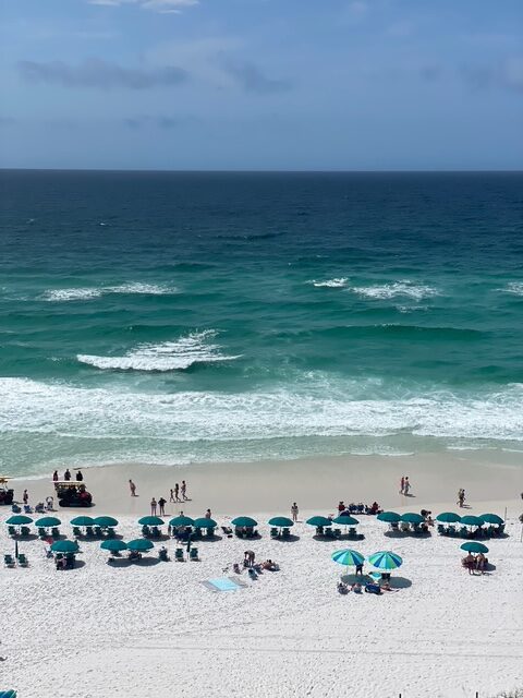 view of gulf of america and the beach in front of jade east towers in destin florida. umbrellas and chairs are set up in rows.