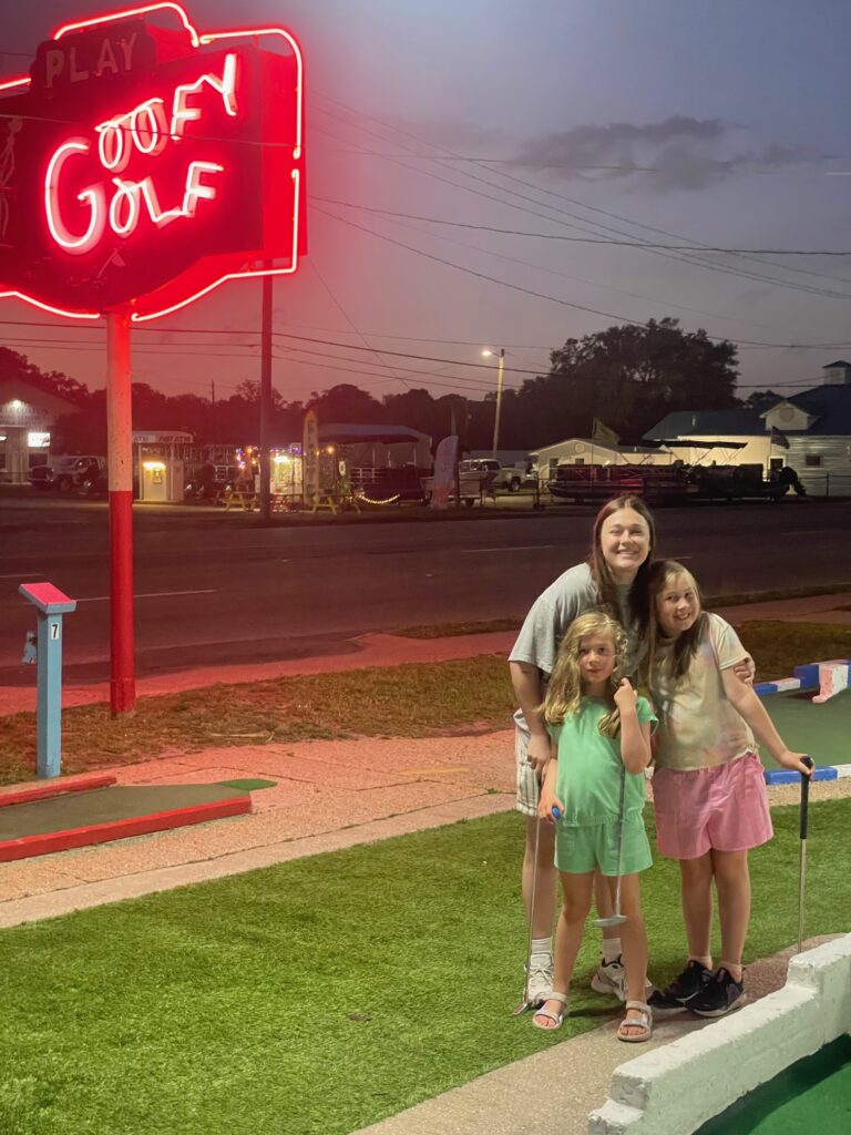 Three sisters posing beside the Goofy Golf sign in destin Florida