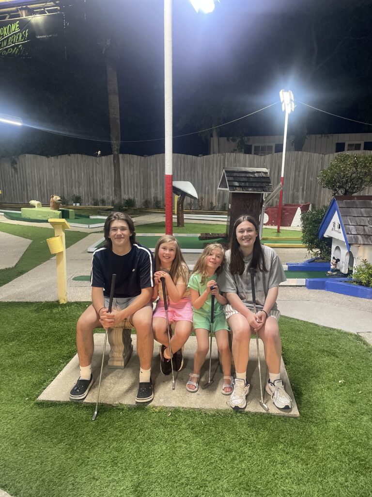 Four siblings sitting on a bench at Goofy Golf in Destin Florida