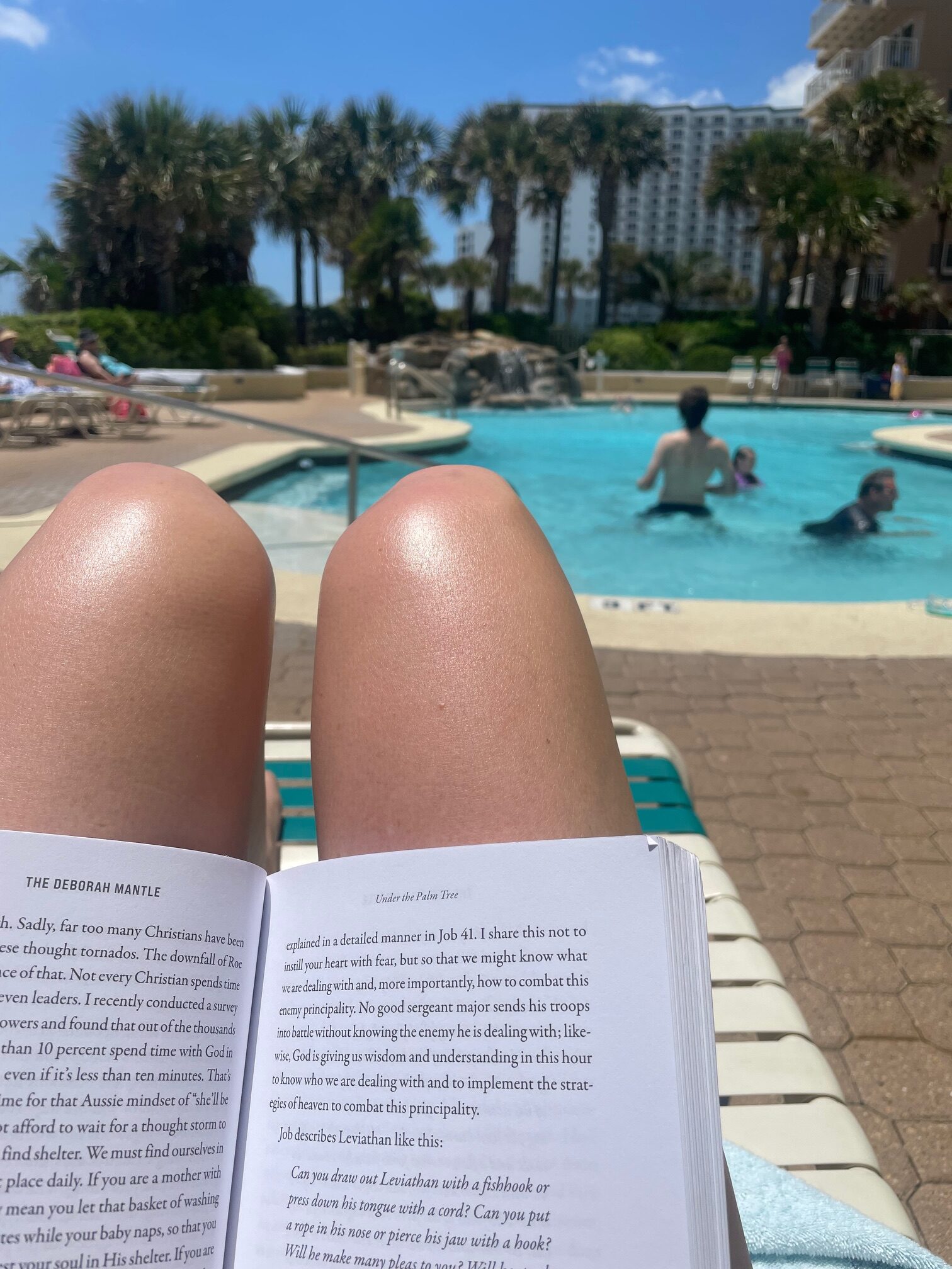 view of lady'sknees with a book on them and the pool is in the background