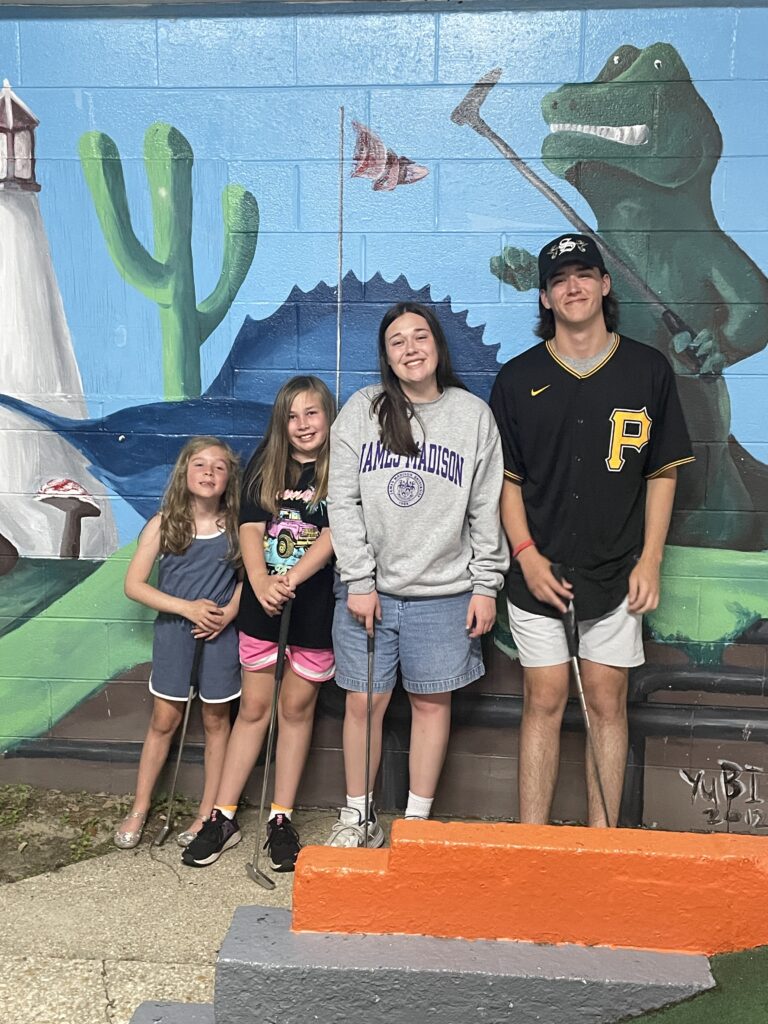 four siblings standing against a mural at Goofy Golf in Destin Florida