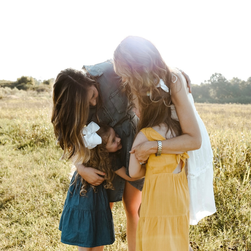 Mom hugging three younger girls in a field