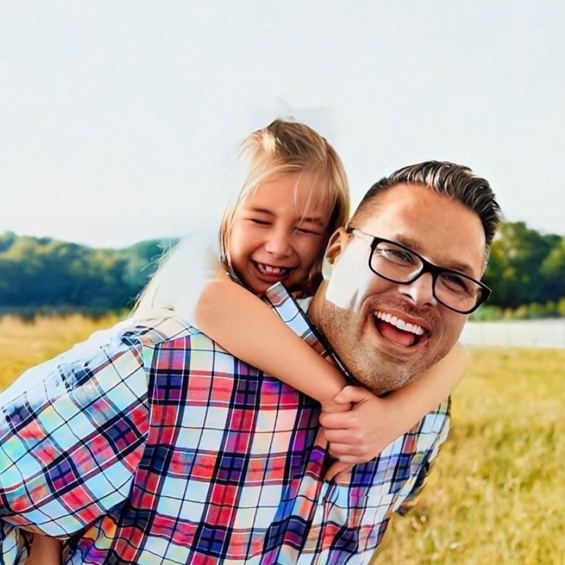 Dad giving young daughter a piggy back ride in a field