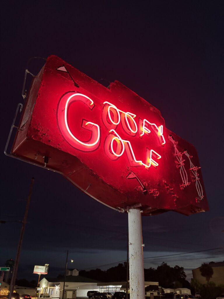 Neon sign at night that says Goofy Gold in red lights