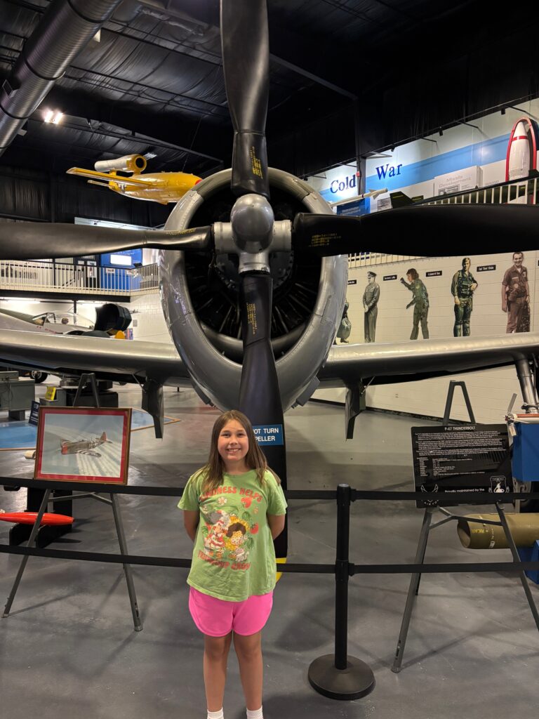 young girl in front of airplane with propeller inside of a museum